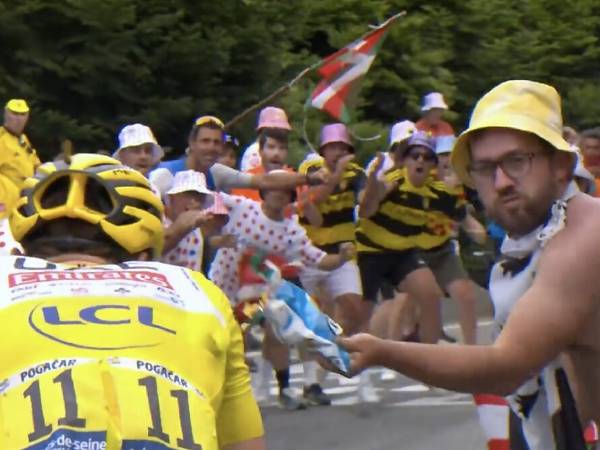 Seorang penggemar bertopi kuning (kanan) melemparkan keripik ke arah Tadej Pogacar di tengah etape 14 Tour de France pada Sabtu (13/7). (Foto: AFP)